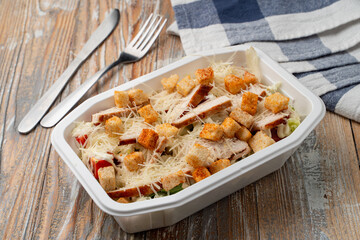 Food delivery: classic caesar salad with grated cheese and grilled chicken in a plastic box with no lid