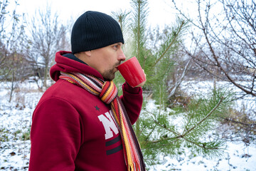 A man drinks coffee or tea outside on a frosty day. Snow all around