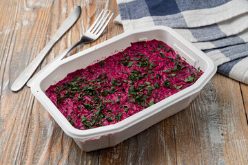 Food delivery during pandemic: herring under the coat in a plastic box on light wooden table