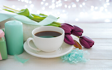 A cup of coffee, candles, flowers on a light background with a burning garland. Side view with copy space. The concept of holidays, March 8.