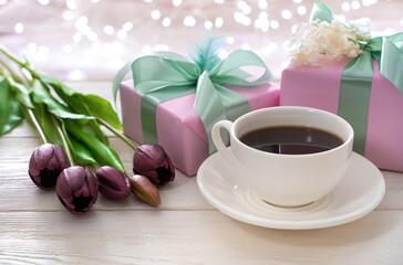 Festive atmospheric background with a cup of coffee, flowers and gift packaging on the background of a burning garland. Side view. The concept of holiday backgrounds.