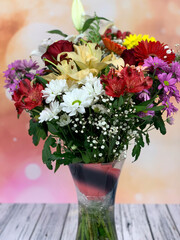 Bouquet of flowers varied in a glass vase on a background of sparkles and a wooden base