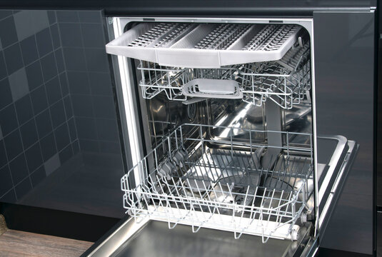 view of the inside of the dishwasher with empty nets for kitchen utensils, against the background of a dark kitchen