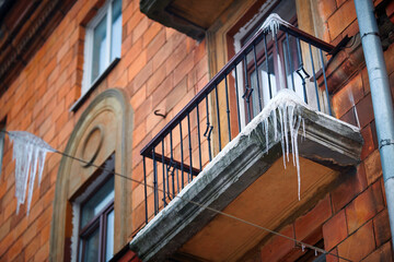Sharp icicles hanging down on balcony and building facade of old residential building. Sharp icicles on facade of building, dangerous icicles over the road where pedestrians walk, risk of  injury