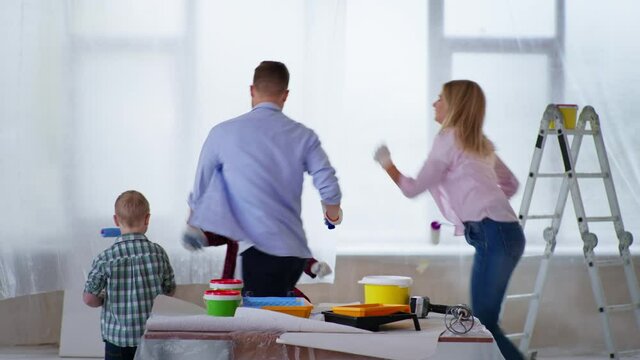 family renovation, young joyful parents with their daughter and son with down syndrome with building tools for painting walls in their hands rejoicing in room at construction site