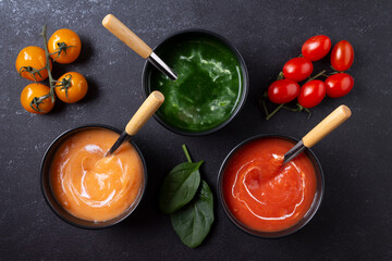 Plates of vegetarian soups: tomato, carrot, spinach. On a black background. Flat lay.