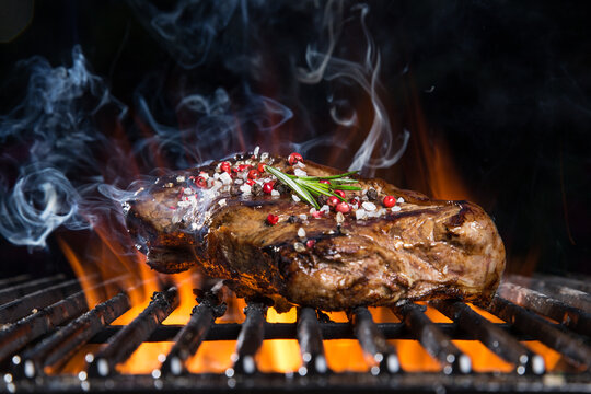 Tasty beef steak on cast iron grate with fire flames. Barbecue concept.