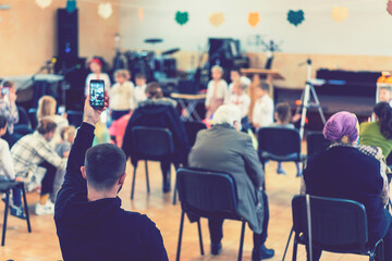 Parents at the performance of children in kindergarten or school. Children on stage. Many parents are watching the kids performance in the hall during Chistmas holiday, blur. toned