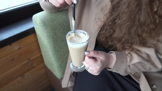 A girl drinks a latte in a coffee shop. Latte with a straw. Drinks a latte from a straw.