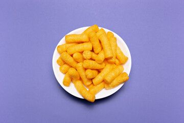 Top view of white bowl with corn puffs on purple background.