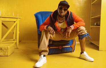 Rapper posing in chair in studio with yellow tones - obrazy, fototapety, plakaty