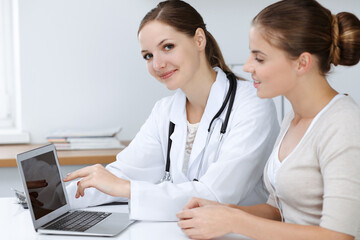 Doctor and patient are sitting and discussing health examination results while using laptop computer. Health care, medicine and good news concepts