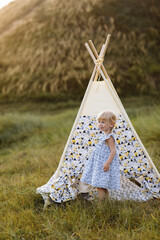 cute little girl is having fun near wigwam in a summer field on sunset. Young family spending time together on vacation, outdoors. The concept of summer holiday. © Andriy Medvediuk