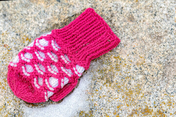 A pink child's mitten lost on the ground next to a small amount of snow. View from directly above.