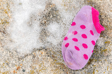 A single lost child's sock lying on the ground. The sock is small and purple, with a small amount snow next to it. View directly down from above.