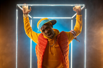 Young stylish rapper poses in illuminated cube - obrazy, fototapety, plakaty