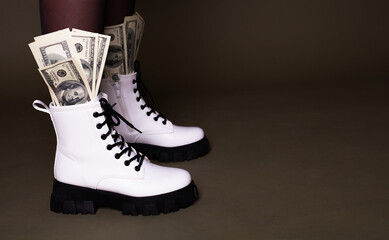 Close up view of dollar bills in shoes on dark background.Boots full of money on a dark background. Image isolated on dark green studio background.
