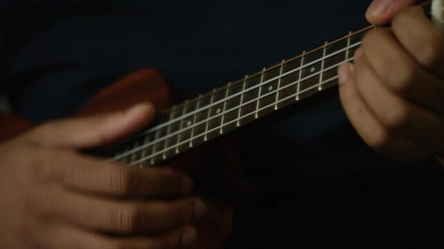 Male hands playing the strings of the ukulele in a tight shot