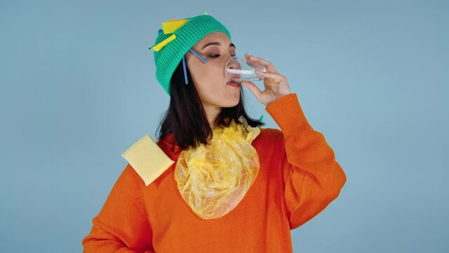 Asian woman with garbage on herself drinking water from plastic cup and throwing it. Looking at the camera.