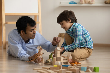 Excited little son and loving dad of indian ethnicity have fun play toys on warm floor at living...