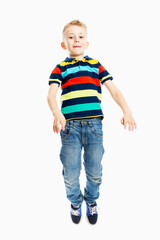 A boy in jeans and a multicolored T-shirt is jumping. White background. Vertical.