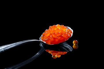 Red caviar in the spoon on black background with reflection