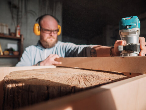 bearded carpenter working with an electric fraser. carpentry workshop. wood stump processing