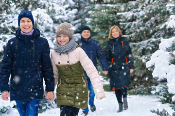 family walking in the winter forest, two parents and two children, beautiful nature with bright snowy fir trees