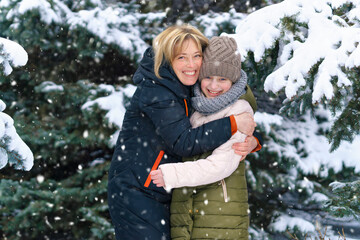 mother and daughter family portrait in a winter forest, one parent and one children, beautiful nature with bright snowy fir trees