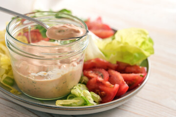 Salad dressing from skyr on a spoon and in a glass jar on a plate with slices of lettuce and tomatoes, healthy raw food meal