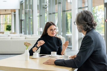 Contemporary elegant businesswoman in eyeglasses sharing ideas with colleague