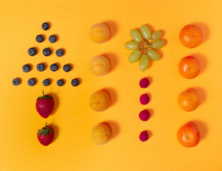 Arrangement of six different fresh organic fruit s- blueberries, strawberries, apricots, raspberries, green grapes, tangerines. Flat lay with yellow background.