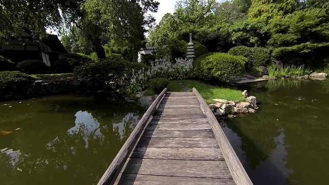 Steadicam shot crosses foot bridge of pond up to stone pagoda, flowers and Japanese lantern.