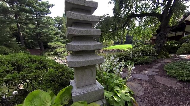 Steadicam shot moving through Japanese garden past stone pagoda and weeping cherry tree to view of exterior of house.