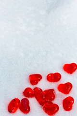 Set of small bright red glass hearts on powdery snow of snowdrift at cold winter day, symbol of romantic love, St. Valentine's Day holiday concept, top view vertikal image witth copy space