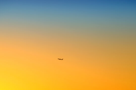 a plane in the distance flies in the sky at sunset