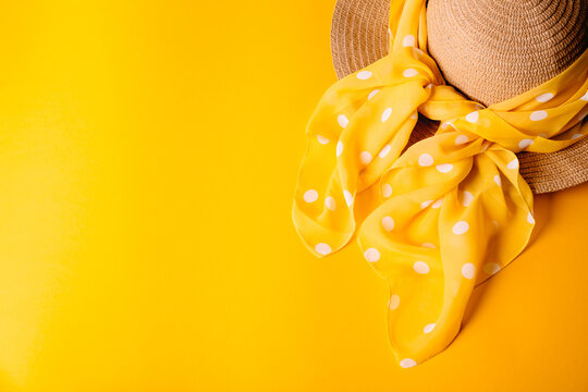 Banner with a straw hat with a polka dot scarf on a yellow background with copy space for advertising and text place. Travel agency. Fashionable head accessoire. Sea vacation in summer time. Gentle