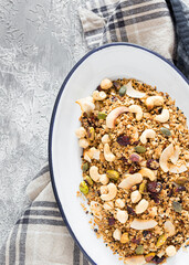 Partial view of a metallic white tray full of delicious granola over a rustic napkin on a white and grey background.