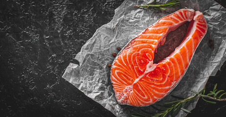 fresh raw salmon steak with aromatic herbs on the dark background