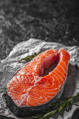 fresh raw salmon steak with aromatic herbs on the dark background
