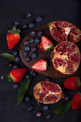 Strawberries, blueberries and pomegranates exposed on a wooden board in dark background.