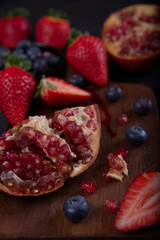 Strawberries, blueberries and pomegranates exposed on a wooden board in dark background.