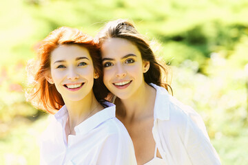 Fototapeta premium Portrait of two cheerful young women standing together and looking at camera over green spring background.