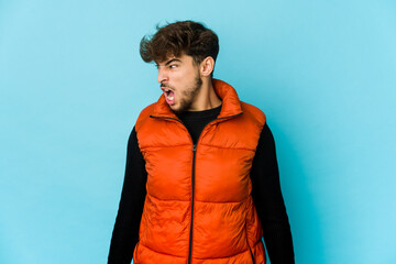 Young arab man on blue background shouting very angry, rage concept, frustrated.