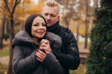 A man hugs and holds the hand of his girlfriend as she smiles