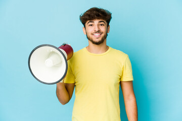 Young arab man holding a megaphone happy, smiling and cheerful.