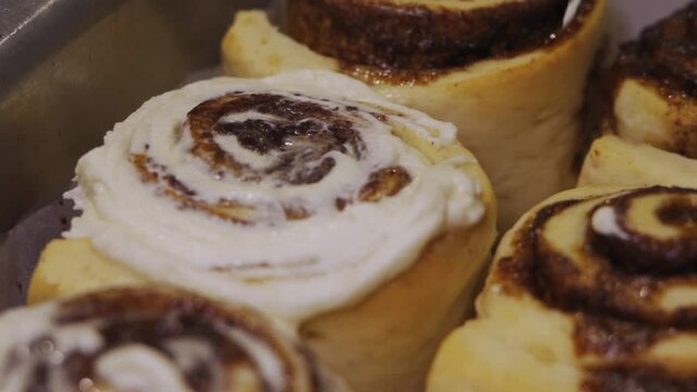 Adding Frosting To Freshly Baked Cinnamon Rolls - high angle, close up
