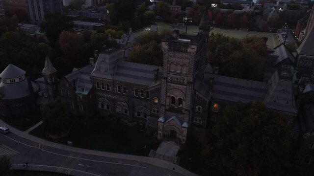 2.7k Aerial orbit around U of T building revealing sports field with people playing spikeball at night under the lights