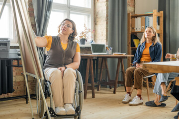 Young disable business coach sitting in front of whiteboard and pointing at it