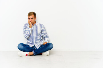 Young caucasian man sitting on the floor who feels sad and pensive, looking at copy space.